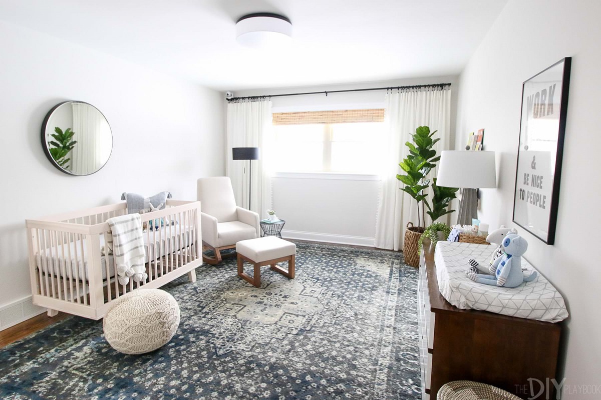 اتاق خواب نوزاد مدرن و شیک با تخت نوزاد چوبی و مبل شیردهی که روی کفپوش چوبی آن، فرش بزرگ زیبایی پهن شده است